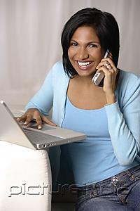 PictureIndia - woman sitting on couch using laptop and talking on mobile phone