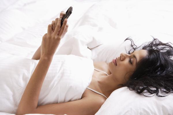 PictureIndia - Indian woman laying down in bed looking at phone.