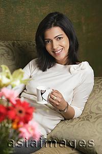 Asia Images Group - woman holds cup of tea and smiles at camera