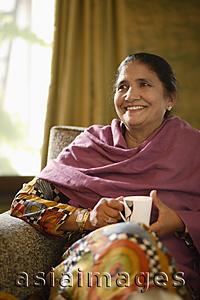 Asia Images Group - older woman sitting on couch, holding tea