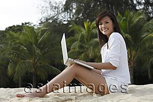 Asia Images Group - Young woman working on laptop on beach