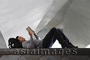 Asia Images Group - man lying down laying at back pack, reading a book
