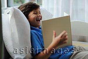 Asia Images Group - Young boy looking at book and laughing