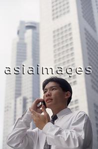 Asia Images Group - Male executive talking on cellular phone with office buildings behind, low angle view
