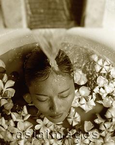 Asia Images Group - Woman in bath with floating flowers, head under running water