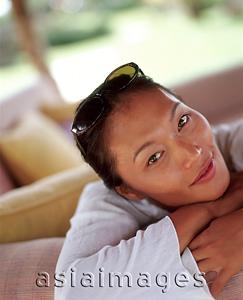 Asia Images Group - Woman relaxing on sofa outdoors, smiling.
