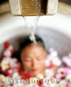 Asia Images Group - Water pouring on head of woman in bathtub with flower petals