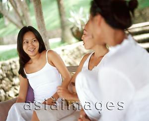 Asia Images Group - Three women wearing white, sitting together on bench talking