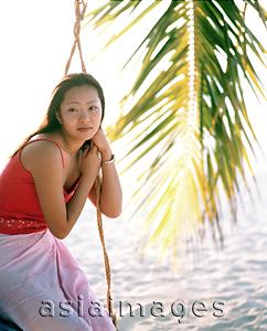 Asia Images Group - Woman sitting on swing looking off camera, coconut frond in background