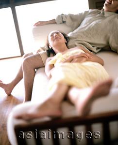 Asia Images Group - Man sitting on sofa, woman lying down with head on lap, defocused
