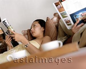 Asia Images Group - Woman and man reading magazines on couch, cups in foreground