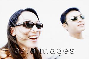 Asia Images Group - Young woman with sunglasses laughing, man in background