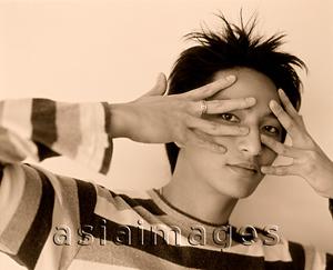 Asia Images Group - Young man peering through splayed fingers.