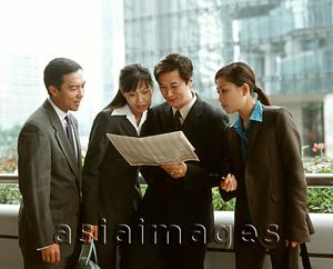 Asia Images Group - Male and female executives sharing newspaper, buildings in background.