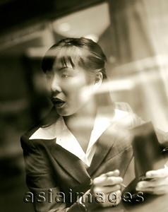 Asia Images Group - Female executive using PDA seen through glass window.