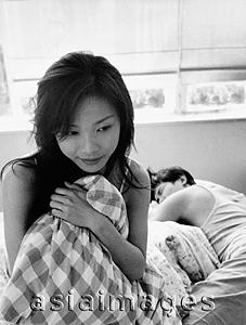 Asia Images Group - Woman clutching pillow, man sleeping in the background