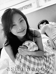 Asia Images Group - Woman clutching pillow, man sleeping in background, portrait