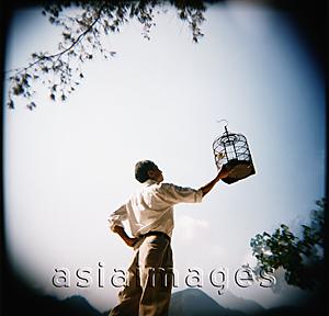 Asia Images Group - Man holding up birdcage