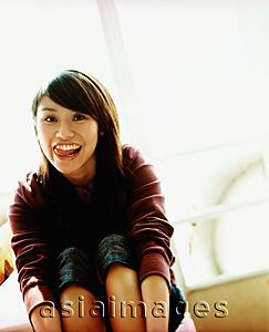 Asia Images Group - Young woman sitting, smiling and sticking out tongue, portrait.