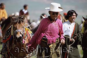 Asia Images Group - China, Szechuan (Sichuan), Kham region, Nomad man in traditional silk shirt leading horse at summer festival.