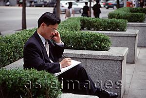 Asia Images Group - Man in business suit, using mobile phone and writing on note pad