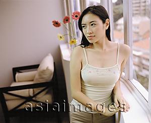 Asia Images Group - Young woman standing by window.