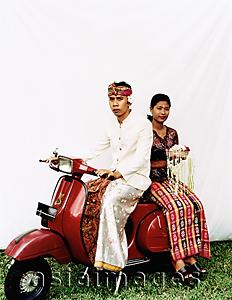 Asia Images Group - Indonesia, Bali, Ubud, Balinese wedding couple in ceremonial dress, sitting on motor scooter, woman carrying offering.