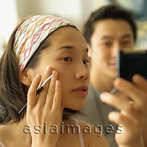 Asia Images Group - Woman touching face, looking at mirror, man in the background looking on.