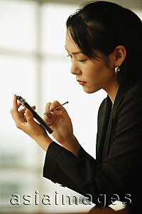 Asia Images Group - Young woman sitting at desk, using PDA