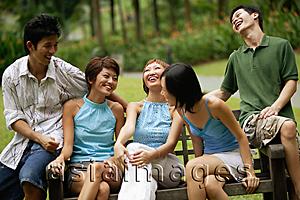 Asia Images Group - Friends sitting side by side on park bench, laughing