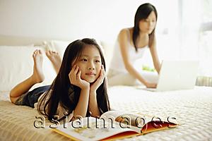 Asia Images Group - Mother and daughter in bedroom, mother using laptop, daughter lying down with book open in front of her