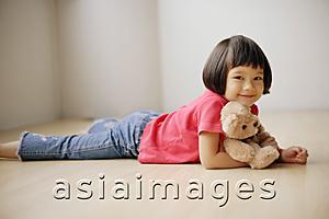 Asia Images Group - Young girl lying on front, hugging teddy bear.