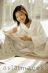 Asia Images Group - Young woman drinking coffee, newspaper open in front of her