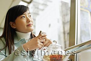 Asia Images Group - Young woman at cafe, holding mobile phone, looking away