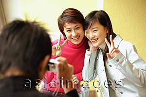 Asia Images Group - Young man holding camera, two women posing for picture, making peace sign