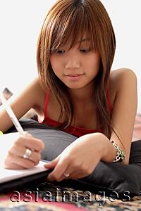 Asia Images Group - Young woman lying on floor, writing in book