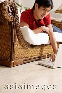 Asia Images Group - Man lying on sofa, using laptop resting on floor