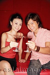 Asia Images Group - Couple sitting side by side, holding drinks, looking at camera