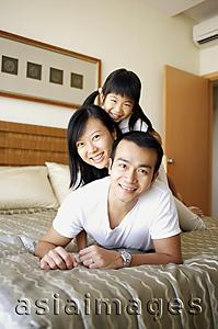 Asia Images Group - Father, mother and daughter lying on bed, looking at camera