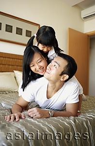 Asia Images Group - Father, mother and daughter lying on bed, on top of one another