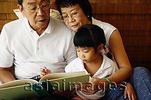 Asia Images Group - Grandparents with granddaughter, reading a book