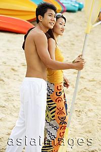 Asia Images Group - Couple on beach holding kayak paddle, looking away