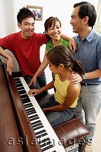Asia Images Group - Family with two children, standing around piano, daughter playing piano