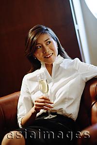Asia Images Group - Woman sitting on sofa, holding glass on champagne, looking away
