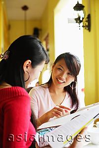 Asia Images Group - Young women with newspaper, smiling at each other