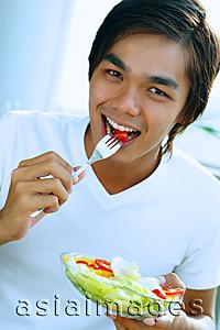 Asia Images Group - Young man looking at camera, eating salad