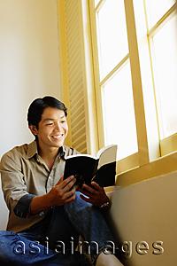Asia Images Group - Man sitting, reading book, smiling