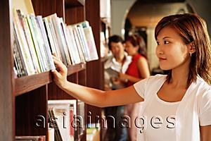 Asia Images Group - Young woman at bookstore, looking at books on shelf