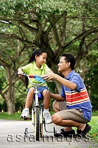 Asia Images Group - Girl on bicycle, father crouching down next to her