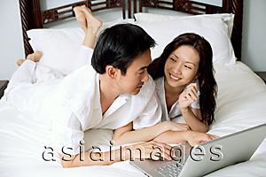Asia Images Group - Couple lying side by side on bed, using laptop